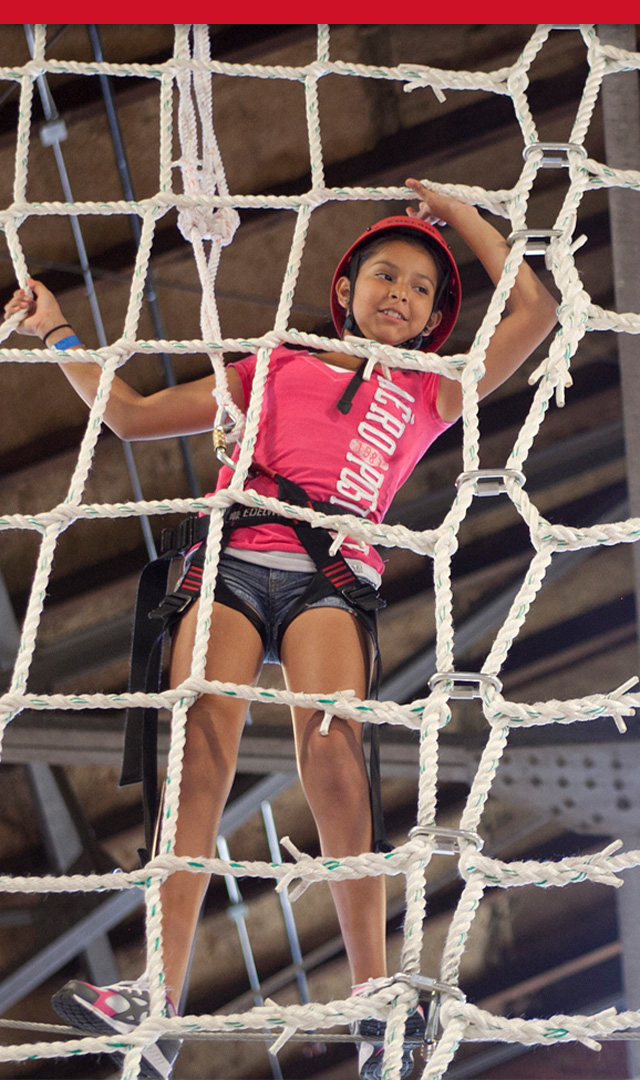 Young female Scout climbing a rope net high in the air