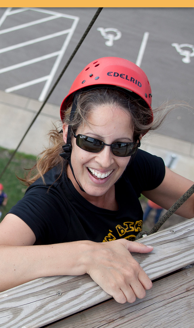Female adult leader smiling as they reach the top of the climbing tower
